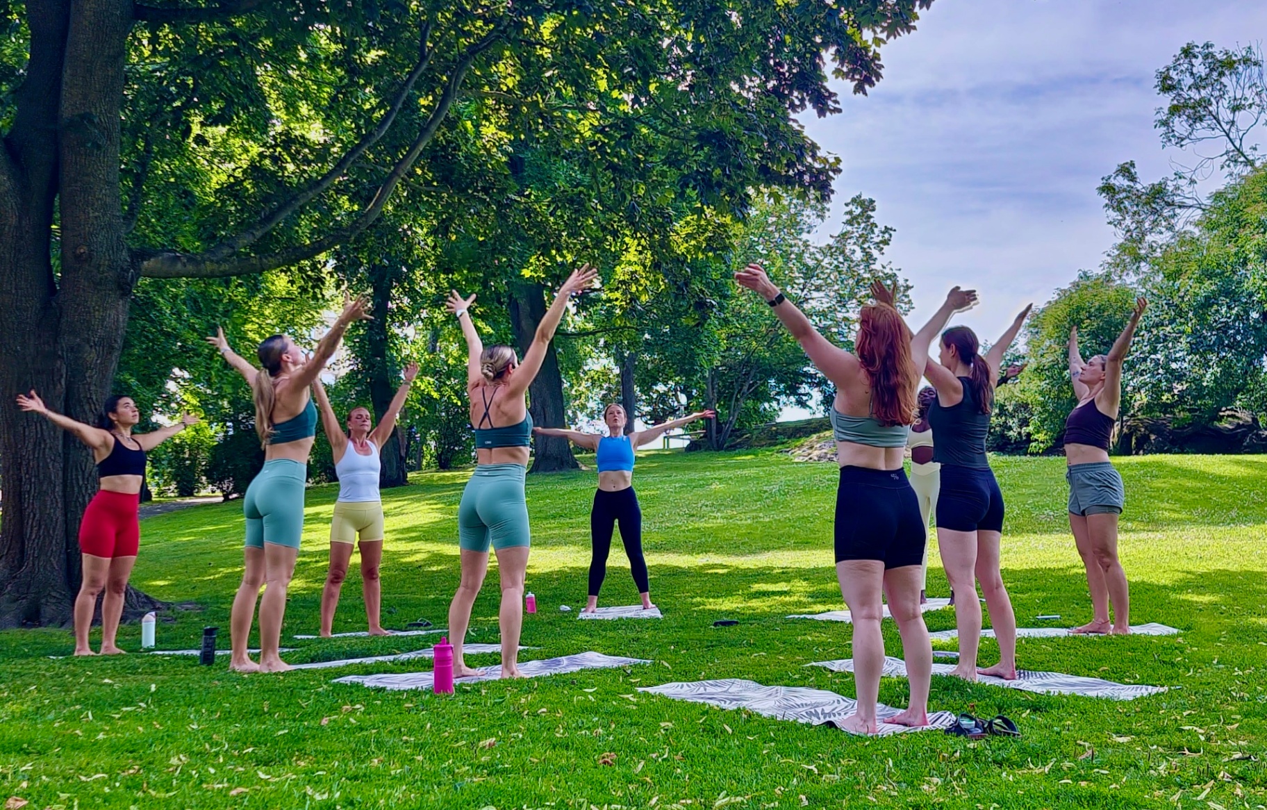 Women practicing yoga together outdoors beneath a canopy of trees