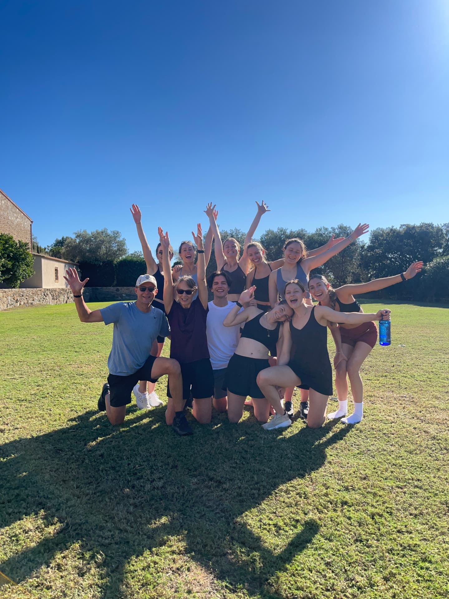 A ROOT outdoor group strength session — a group of twelve celebrating together on a sunlit lawn